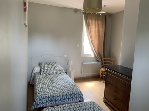 Bright cottage bedroom at Gites Mas D'en Ratéro in Thuir with twin beds, wooden dresser, and window with mountain views