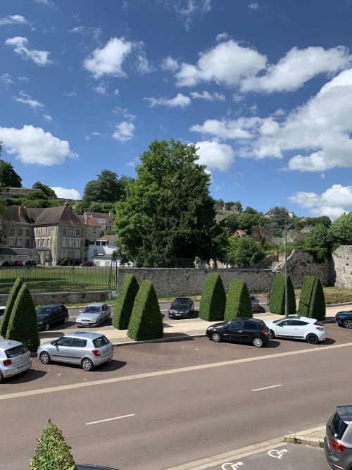 Parking des Remparts de Joussaume Latour à Château-Thierry avec topiaires, bâtiments historiques et ciel bleu