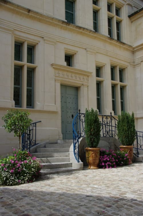 Élégante entrée en pierre des Remparts de Joussaume avec porte bleue, balustrades ornementales et plantes fleuries à Château-Thierry