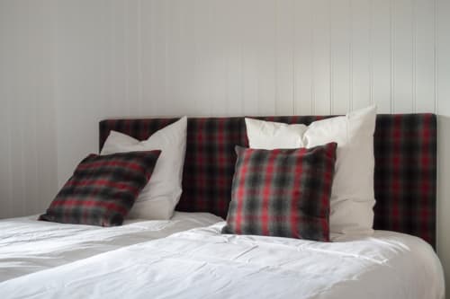 Chalet Domisiladoré bedroom with plaid red and black pillows on white bedding against wood headboard