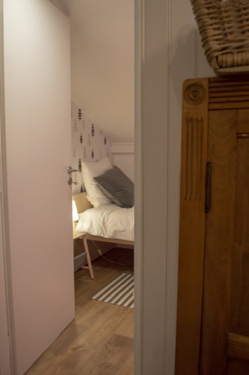 Entrée de chambre au Chalet Domisiladoré avec lit à linge blanc et tête de lit motif plumes, armoire en bois, style rayé