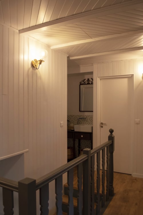 Upstairs hallway at Chalet Domisiladoré with wooden railings, white walls, and bathroom entrance in Haute-Savoie, France