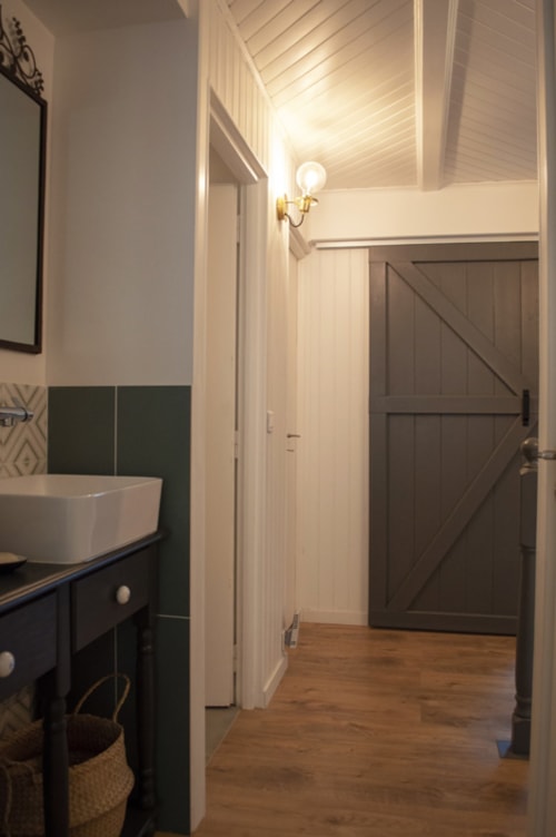 Modern bathroom hallway at Chalet Domisiladoré with green tile accents, white vessel sink, and barn door entry