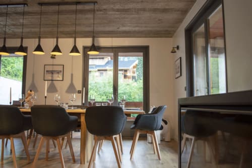 Modern dining room at Chalet Domisiladoré with wooden table, black chairs, pendant lights, and mountain views through glass