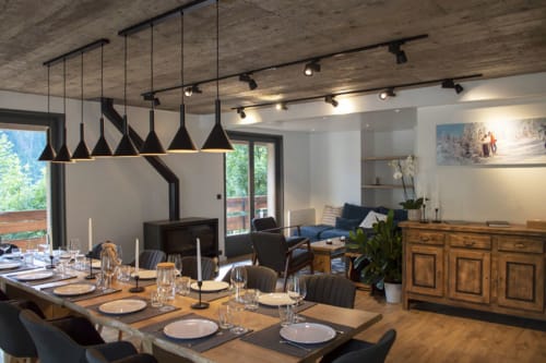 Modern dining room at Chalet Domisiladoré with black pendant lights, wooden table, and living area view