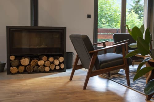 Modern fireplace with wood storage, mid-century armchair, and potted plant in Chalet Domisiladoré's lounge area