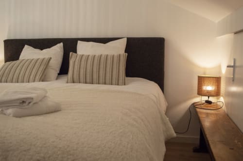 Modern bedroom at Chalet Domisiladoré with dark headboard, cream bedding, striped pillows, and warm bedside lamp