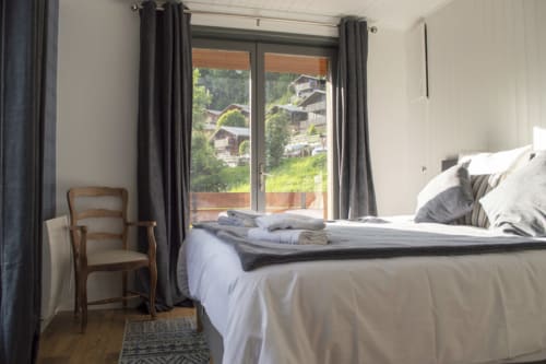 Bright mountain view bedroom at Chalet Domisiladoré with bed, armchair, and balcony overlooking alpine landscape