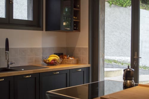 Modern black kitchen with wooden countertop, bananas and fruit basket, alpine views through glass doors at Chalet