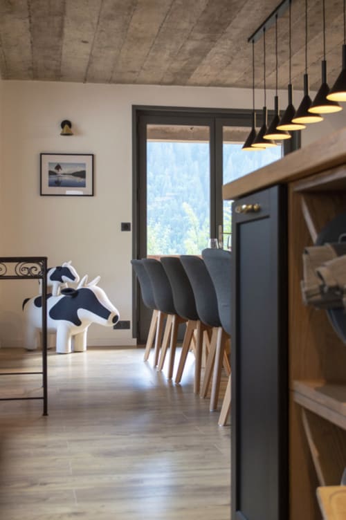 Modern mountain chalet dining area with gray chairs, pendant lights, concrete ceiling, and alpine views through glass doors