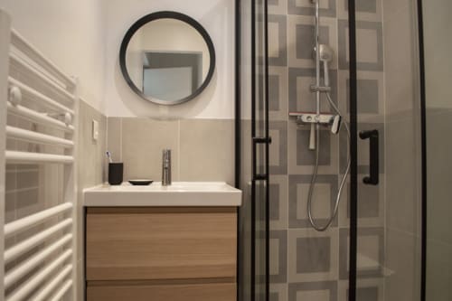 Modern bathroom in Chalet Domisiladoré with round mirror, wooden vanity, and walk-in shower with geometric tile design