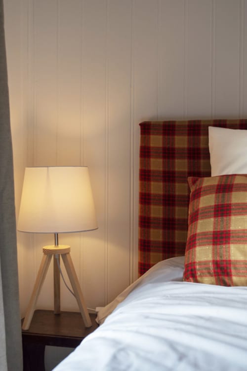 Cozy bedroom at Chalet Domisiladoré with tripod lamp, plaid bedding, and white walls
