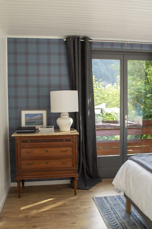 Bedroom at Chalet Domisiladoré with wooden dresser, white lamp, plaid wallpaper, black curtains, and mountain views through