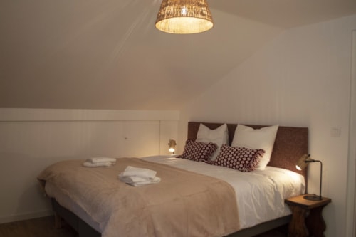 Modern bedroom at Chalet Domisiladoré with queen bed, brown headboard, white bedding, decorative pillows, ceiling lamp, and