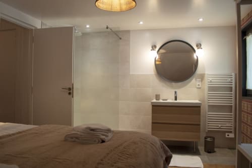 Modern ensuite bedroom at Chalet Domisiladoré with circular mirror, wood vanity, glass shower enclosure, and heated towel