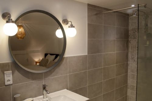 Modern bathroom at Chalet Domisiladoré with circular mirror, sconce lighting, and glass shower enclosure