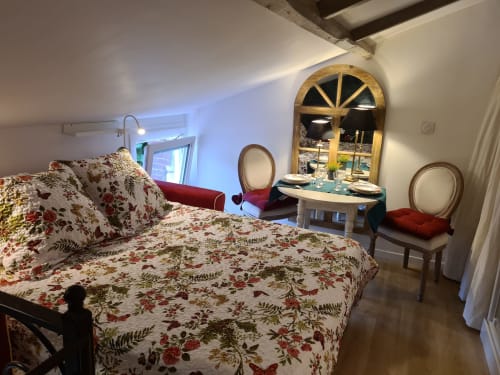 La chambre studio du Petit Nid d'Aigle à Giverny avec literie fleurie, vue jardin par fenêtre cintrée et coin repas