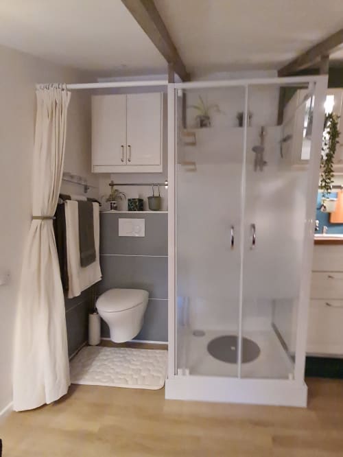 Salle de bain compacte avec toilettes, lavabo, rangements blancs et douche vitrée dépoli au gîte Le Petit Nid d'Aigle