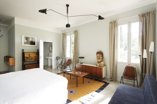 Mas De Lafeuillade bedroom in Montpellier with mid-century furniture, white bed, wooden desk, and large windows with cream