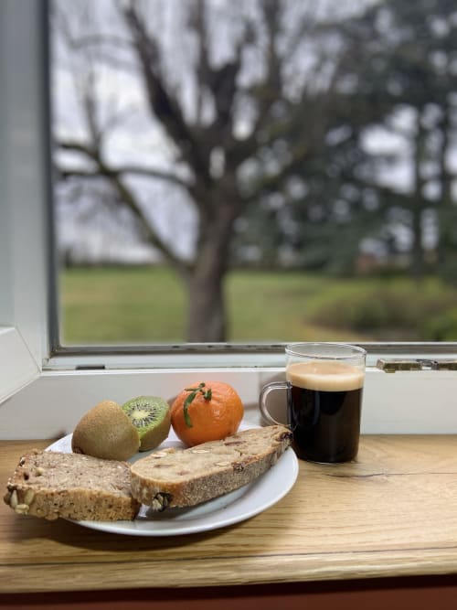 Petit-déjeuner au Château de Grandmont : pain complet, kiwi, orange et café noir sur le rebord de la fenêtre avec vue sur Blacé