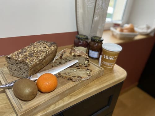 Petit-déjeuner au Château de Grandmont : pain aux graines, fruits frais, confiture et miel sur plateau en bois à Blacé