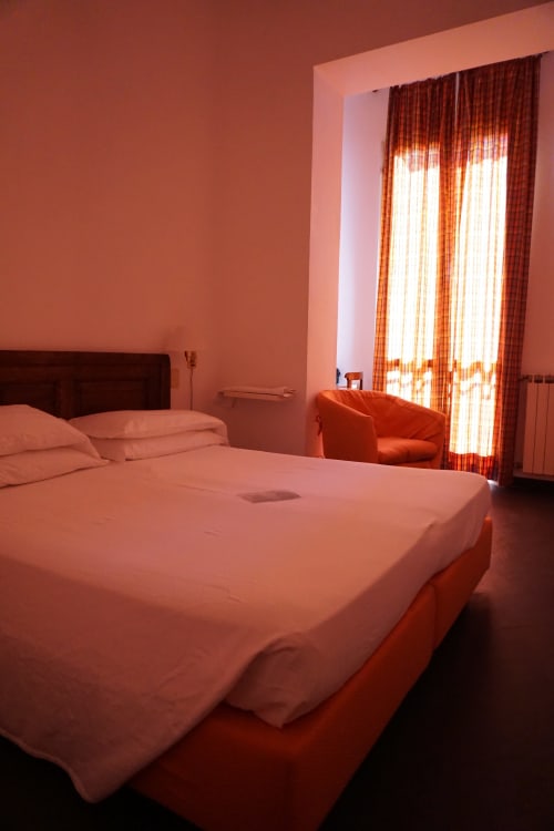 Helles modernes Zimmer im Hotel Beau Rivage in Alassio mit Meerblick, rotem Bett, orangefarbenen Vorhängen und natürlichem Licht