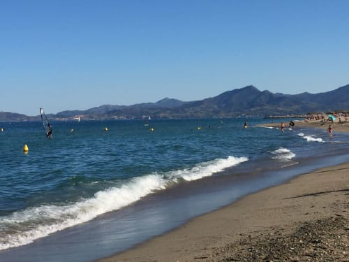 Plage de sable fin avec une eau bleu clair, montagnes et baigneurs près de Thuir, France