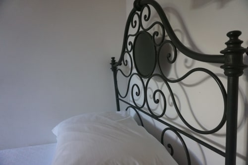 Verzierte schwarze Metallbettkopfteile im Zimmer des Hotel Beau Rivage in Alassio mit weißer Bettwäsche und neutralen Wänden