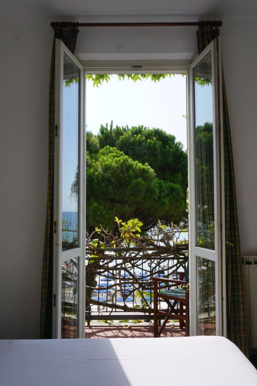 Offene Balkontüren im Hotel Beau Rivage in Alassio mit Meerblick, üppiger Begrünung und mediterraner Küstenlinie vom Schlafzimmer aus