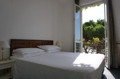 Helles Strandhotelzimmer im Hotel Beau Rivage Alassio mit Meerblickbalkon, weißer Bettwäsche und dunklem Holzbettgestell