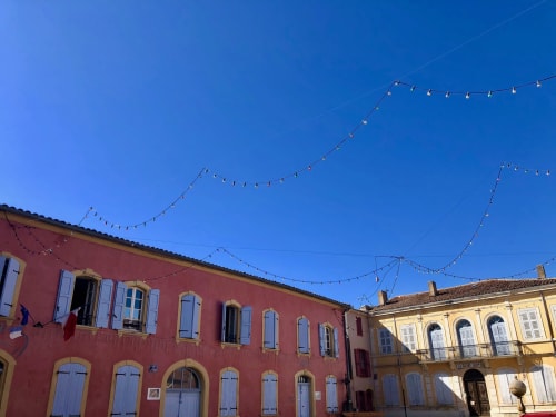 Colorful historic buildings in Montaut with decorative string lights strung across the square under clear blue sky
