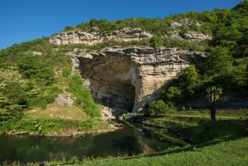 Natural rock arch over river near Montaut, France with green cliffs and lush vegetation