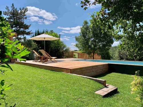 Luxury backyard pool deck with wooden loungers, umbrella, and manicured lawn at Maison Monsieur Léger in Montaut
