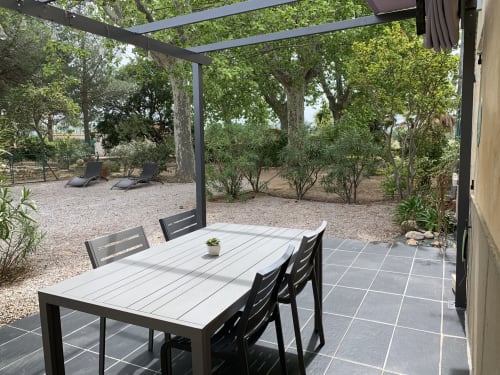 Shaded terrace with dining table at Gites Mas D'en Ratéro cottage in Thuir, surrounded by mature trees and garden furniture