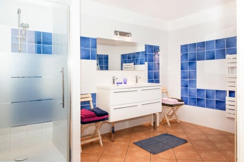 Modern bathroom at Gites Mas D'en Ratéro cottage in Thuir with blue tile walls, white vanity, and shower enclosure