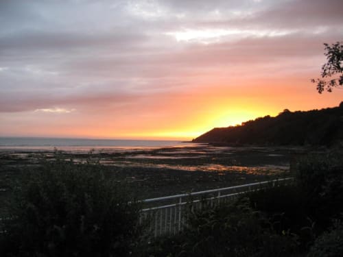 Vue du coucher de soleil depuis l'Abri Des Vents à Saint-Jean-le-Thomas avec océan, falaises et balustrade