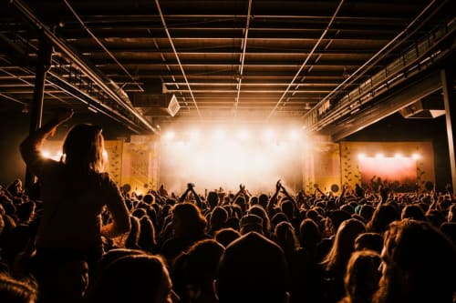 Grand foule lors d'un concert en salle avec éclairages de scène intenses dans un lieu de divertissement de type entrepôt, Saint-Jean-le-Thomas