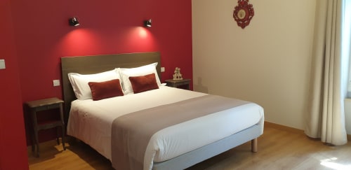 Chambre moderne au Château de Grandmont avec mur d'accent rouge, literie blanche, tête de lit foncée et vue sur le jardin