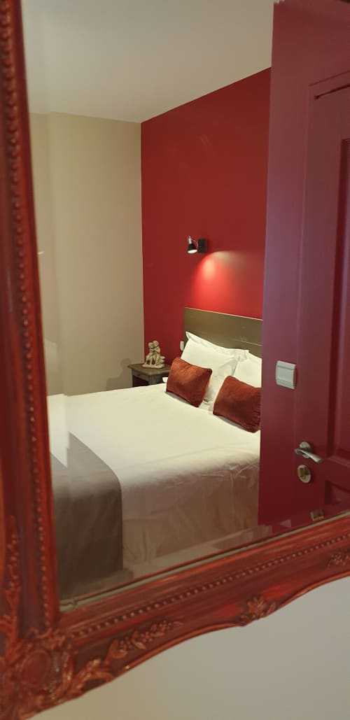 Chambre moderne du Château de Grandmont aux murs rouge profond, literie blanche, coussins bordeaux et éclairage ambiant à Blacé