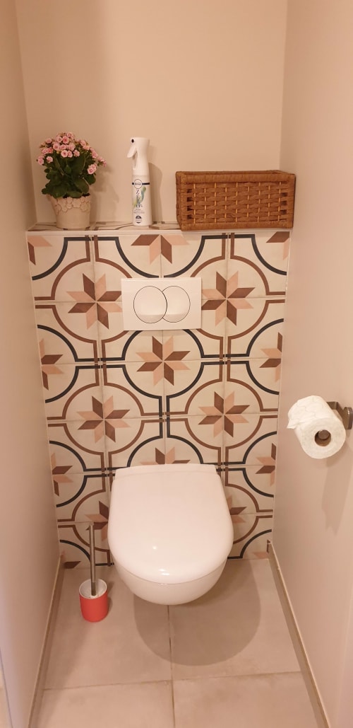 Toilettes du Château de Grandmont avec carrelage décoratif, étagère ornée de fleurs et panier