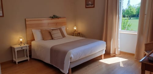 Chambre lumineuse au gîte Château de Grandmont avec lit en bois, fenêtres sur jardin et éclairage chaleureux