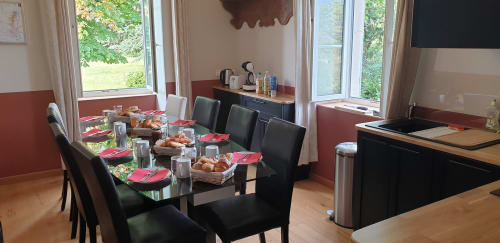Salle à manger du gîte Château de Grandmont avec table noire, serviettes rose, pâtisseries et vue sur le jardin