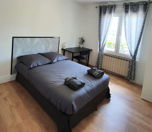 Chambre avec lit foncé, tête de lit grise, bureau, fenêtre avec rideaux et vue sur la ville à NancyRoom Vandoeuvre-les-Nancy