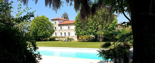 Le Château de Grandmont à Blacé présente une piscine turquoise, une pelouse impeccable et un élégant manoir entouré d'arbres luxuriants.