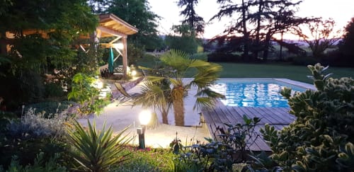 Allée de jardin illuminée menant au pavillon lumineux et à la piscine du gîte Château de Grandmont à Blacé, France, en soirée