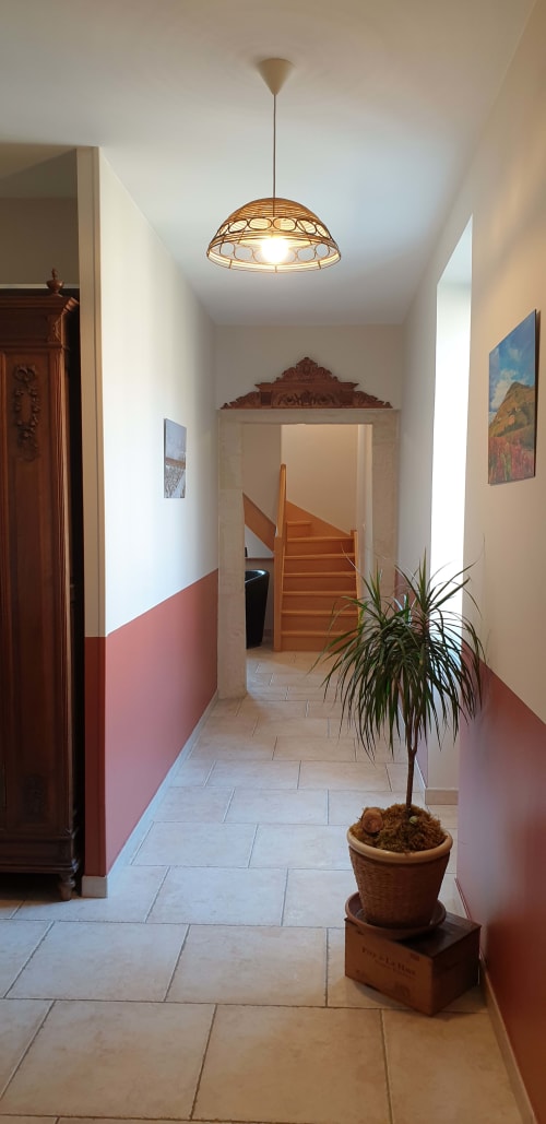 Couloir lumineux du Château de Grandmont B&B à Blacé avec murs roses, escalier en bois, plante en pot et décoration