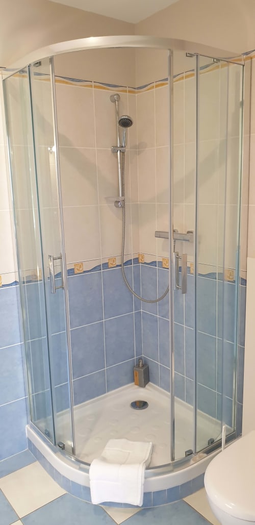 Cabine de douche d'angle moderne aux carrelages bleu et crème du gîte Château de Grandmont, Blacé