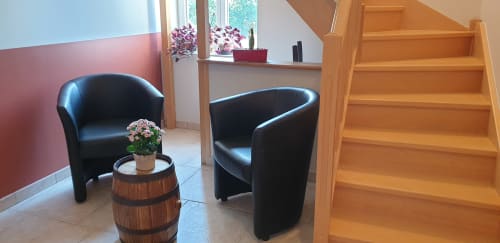 Élégant salon du gîte Château de Grandmont avec fauteuils en cuir noir, table d'appoint en bois et escalier à Blacé