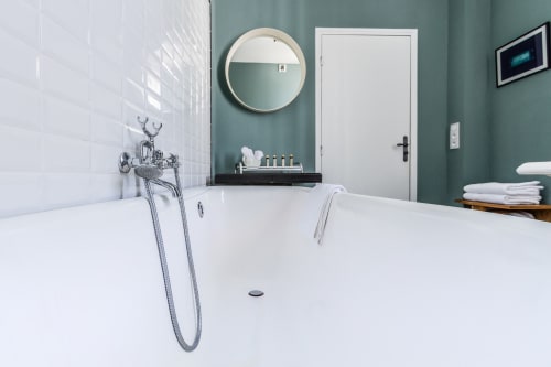 Modern bathroom at Mas De Lafeuillade, Montpellier with white freestanding tub, seafoam walls, and round mirror