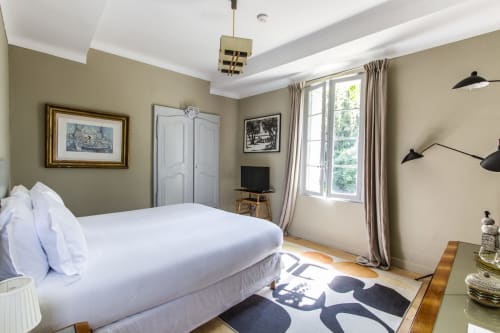 Elegant bedroom at Mas De Lafeuillade B&B in Montpellier with white bed, neutral walls, large windows, and modern black
